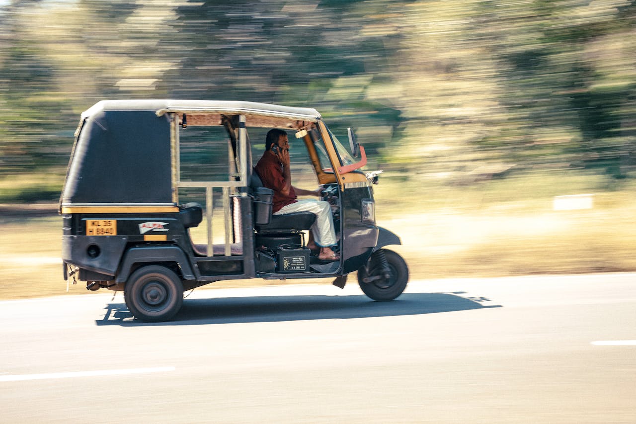 services-04 Auto rickshaw moving at speed with driver using phone on a clear day.