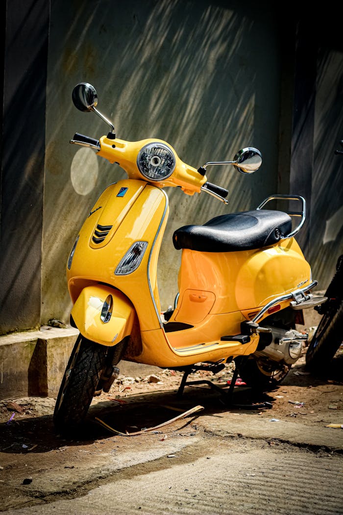A vibrant yellow vintage scooter illuminated by sunlight on a city street in Dhaka.