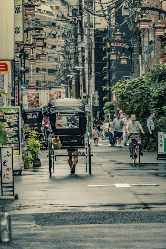 services-01 A lively Tokyo street with a rickshaw and cyclists going past shops and signs.