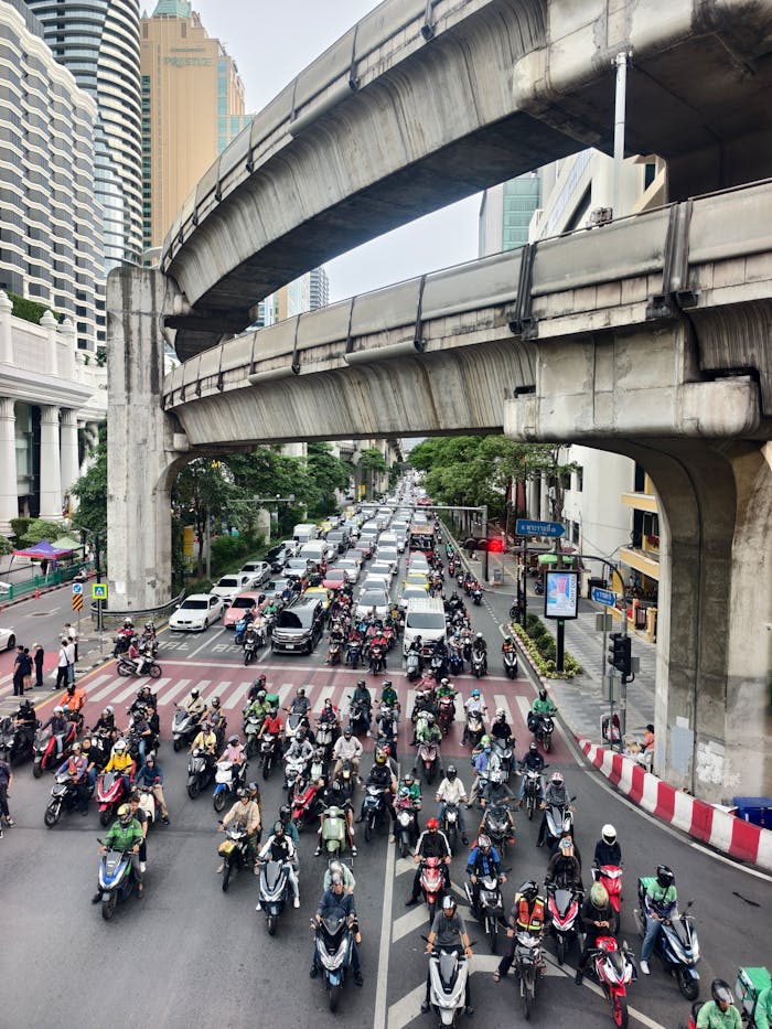 Lively city scene showing a busy Bangkok intersection packed with motorbikes and cars during the day.